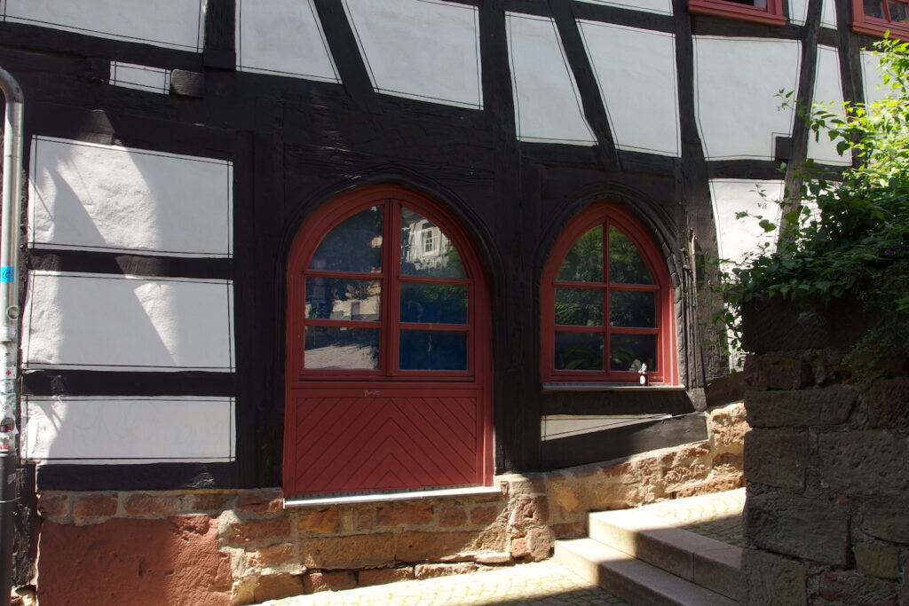 Zwei Bogenfenster. Das linke hat unten einen geschlossenen Teil, der direkt auf dem Sandsteinsockel des Hauses aufliegt.