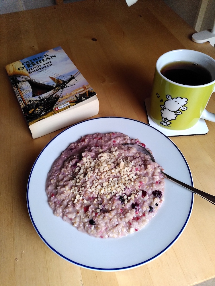 Ein Teller mit Porridge, ein Becher mit schwarzem Tee und das Buch "Duell vor Sumatra" von Patrick O'Brian