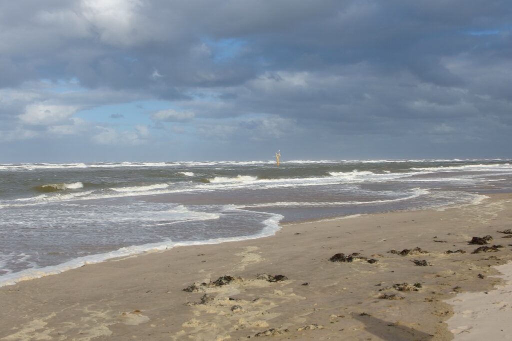 Strand mit auflaufender Brandung, am Himmel hängen dramatisch dunkle Wolken.